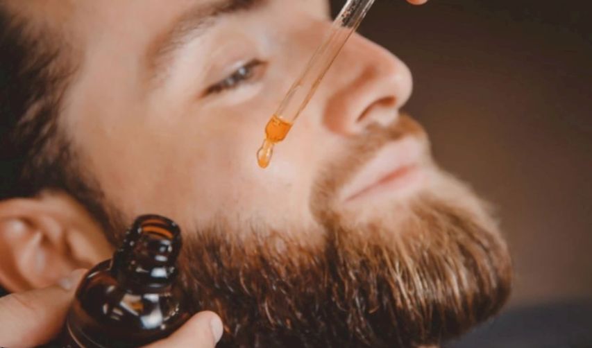 A man is putting beard oil on his patchy beard